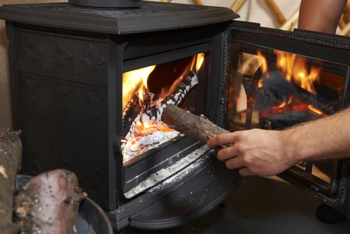 man putting log into wood burning stove